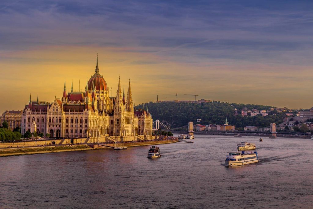 Folyami hajók közlekednek a Dunán a budapesti Parlament előtt naplementében.