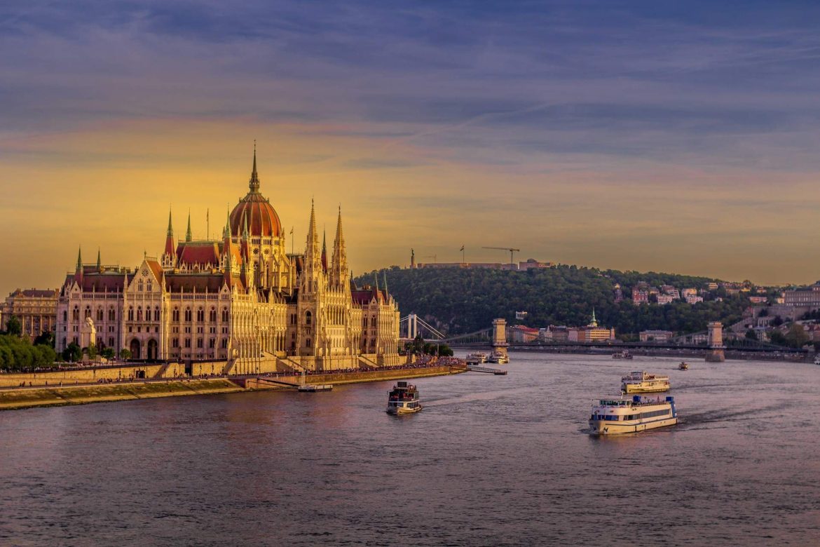 Folyami hajók közlekednek a Dunán a budapesti Parlament előtt naplementében.
